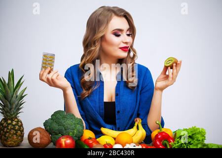 Frau an einem Tisch mit Kiwi und Pillen auf dem Hintergrund von Obst und Gemüse Stockfoto