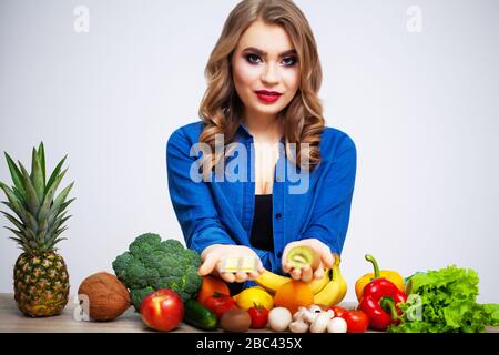 Frau an einem Tisch mit Kiwi und Pillen auf dem Hintergrund von Obst und Gemüse Stockfoto