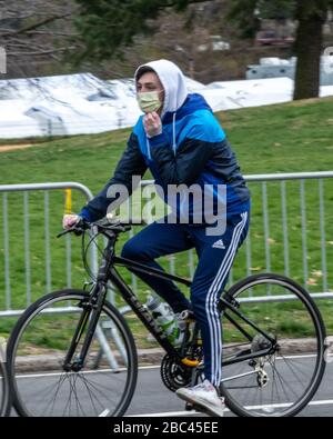 New York, USA. April 2020. Ein junger Mann trägt eine Gesichtsmaske und Handschuhe, während er mit dem Fahrrad an einem provisorischen Krankenhaus vorbeifährt, das in Zelten im Central Park von New York City eingerichtet wurde. Heute sagte die Regierung, dass Newyorkers ihre Gesichter bedecken sollten, wenn sie nach draußen gehen, um eine Ausbreitung des Coronavirus zu verhindern. Kredit: Enrique Shore/Alamy Live News Stockfoto