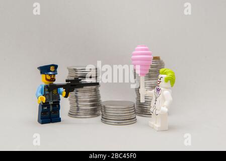 Florianopolis, Brasilien, 28. März 2020: Polizist strebt seine Schusswaffe auf den Joker neben einem Münzhaufen an. Kriminalität zahlt nicht. LEGO-Miniaturen sind Menschen Stockfoto