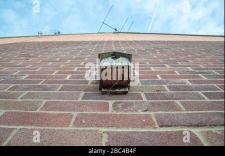 Low Angle View os ein kleines, scheinbar ungenutztes und verwittertes Holzvogelhaus, das an einer ausladenden äußeren Ziegelwand eines typischen Einfamilienhauses in TH befestigt ist Stockfoto