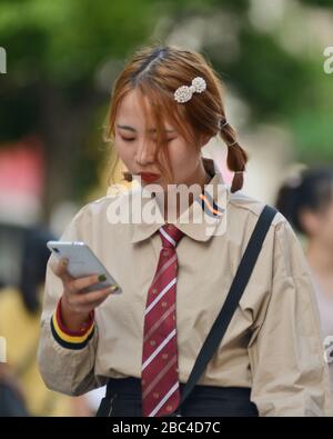 Ein junges chinesisches Mädchen, das ihr Handy in der Jianghan Road, Wuhan, China verwendet Stockfoto