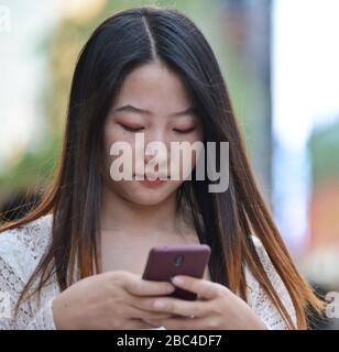 Ein junges chinesisches Mädchen, das ihr Handy in der Jianghan Road, Wuhan, China verwendet Stockfoto