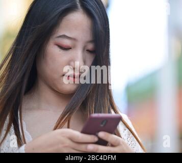 Ein junges chinesisches Mädchen, das ihr Handy in der Jianghan Road, Wuhan, China verwendet Stockfoto