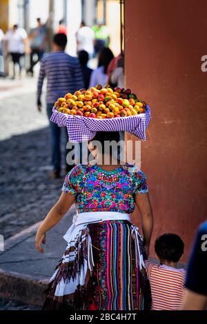 Eine Mutter trägt einen Obstkorb auf dem Kopf, während sie auf den Markt in Antigua, Guatemala geht. Stockfoto