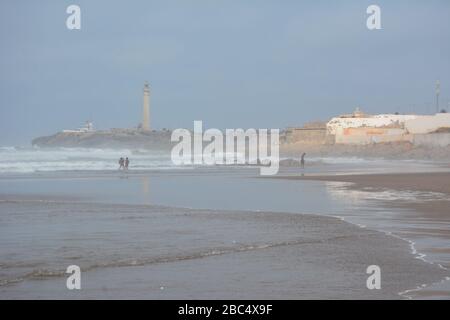 Am öffentlichen Strand von Casablanca, Marokko, mit dem historischen Leuchtturm El Hank, baden und spielen die Einheimischen im Meer. Stockfoto