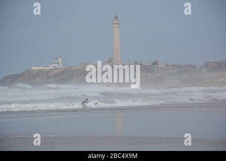 Am öffentlichen Strand von Casablanca, Marokko, mit dem historischen Leuchtturm El Hank, baden und spielen die Einheimischen im Meer. Stockfoto