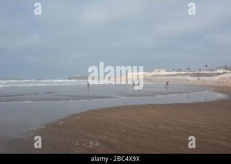 Am öffentlichen Strand von Casablanca, Marokko, mit dem historischen Leuchtturm El Hank, baden und spielen die Einheimischen im Meer. Stockfoto