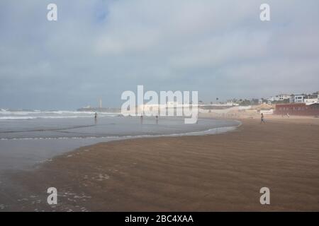 Am öffentlichen Strand von Casablanca, Marokko, mit dem historischen Leuchtturm El Hank, baden und spielen die Einheimischen im Meer. Stockfoto