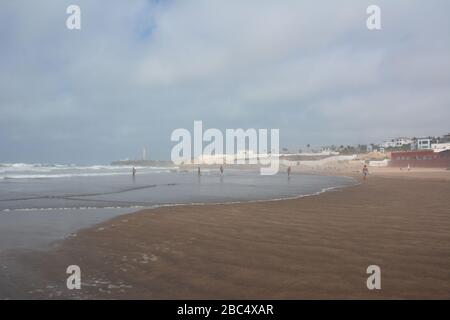 Am öffentlichen Strand von Casablanca, Marokko, mit dem historischen Leuchtturm El Hank, baden und spielen die Einheimischen im Meer. Stockfoto