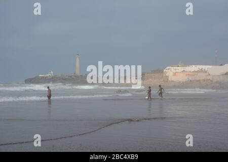 Am öffentlichen Strand von Casablanca, Marokko, mit dem historischen Leuchtturm El Hank, baden und spielen die Einheimischen im Meer. Stockfoto