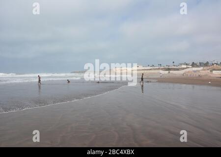 Am öffentlichen Strand von Casablanca, Marokko, mit dem historischen Leuchtturm El Hank, baden und spielen die Einheimischen im Meer. Stockfoto