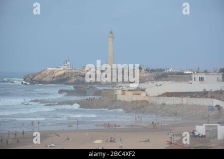 Menschen am öffentlichen Sandstrand von Casablanca, Marokko, mit dem historischen Leuchtturm El Hank im Hintergrund. Stockfoto