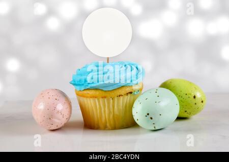 Cupcake Topper Mockup mit einem blauen Milchkuchen umgeben von bunten Ostereiern. Stockfoto