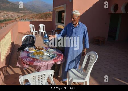 Ein Einheimischer gießt Tee aus einer Stahltapette und bietet traditionelle Gastfreundschaft in einem Dorf in Amazigh Berber in der Nähe von Asni im marokkanischen Atlasgebirge. Stockfoto