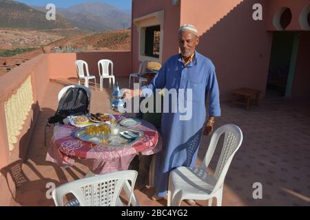 Ein Einheimischer gießt Tee aus einer Stahltapette und bietet traditionelle Gastfreundschaft in einem Dorf in Amazigh Berber in der Nähe von Asni im marokkanischen Atlasgebirge. Stockfoto