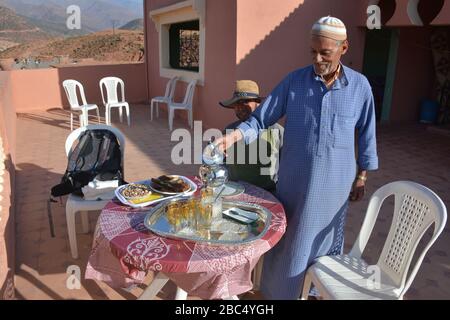 Ein Einheimischer gießt Tee aus einer Stahltapette und bietet traditionelle Gastfreundschaft in einem Dorf in Amazigh Berber in der Nähe von Asni im marokkanischen Atlasgebirge. Stockfoto