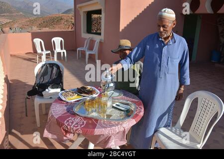 Ein Einheimischer gießt Tee aus einer Stahltapette und bietet traditionelle Gastfreundschaft in einem Dorf in Amazigh Berber in der Nähe von Asni im marokkanischen Atlasgebirge. Stockfoto