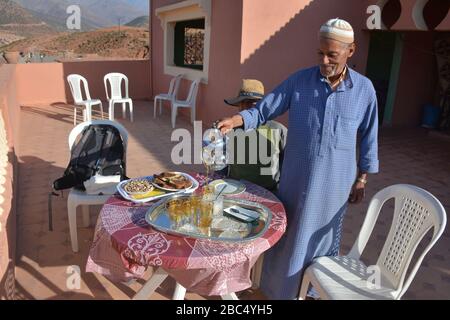 Ein Einheimischer gießt Tee aus einer Stahltapette und bietet traditionelle Gastfreundschaft in einem Dorf in Amazigh Berber in der Nähe von Asni im marokkanischen Atlasgebirge. Stockfoto