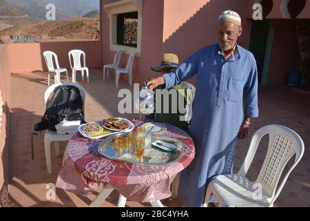 Ein Einheimischer gießt Tee aus einer Stahltapette und bietet traditionelle Gastfreundschaft in einem Dorf in Amazigh Berber in der Nähe von Asni im marokkanischen Atlasgebirge. Stockfoto