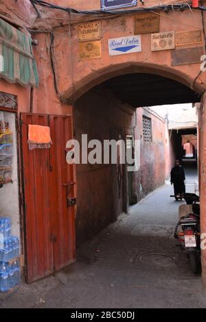 Eine Frau in traditioneller Kleidung nähert sich einem Torbogen entlang einer schmalen Gasse in Marrakesch Medina, Marokko. Stockfoto