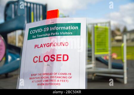 Ein geschlossenes Spielplatzschild für COVID-19 vor einem kleinen Kinderspielplatz. Stockfoto