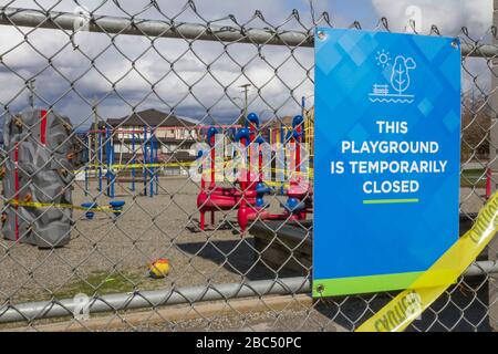 Spielplatz ist vorübergehend geschlossen Schild an Kettengliederzaun mit Spielplatz im Hintergrund Stockfoto