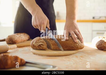 Hände schneiden frisches hausgemachtes Brot auf einem Tisch in einer Backküche. Baker schneidet Brot. Stockfoto