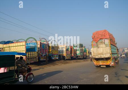 Ein LKW fährt an einer Reihe von Transportfahrzeugen auf dem Obst- und Gemüsemarkt in Lahore, Punjab vorbei. Stockfoto