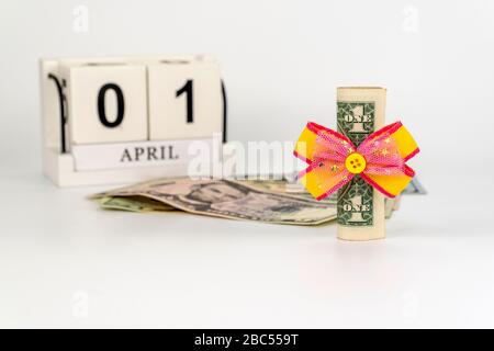 Ständiger Kalender mit Holzwürfeln. Geburtstag des Dollars am 01. April. Dollar mit festlichem Bogen verbunden. Amerikanische Währung, Papierzust Stockfoto