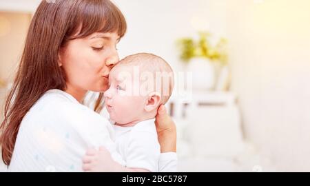 Glückliche Mutter gibt ihrem Säugling einen Kuss auf die Stirn Stockfoto