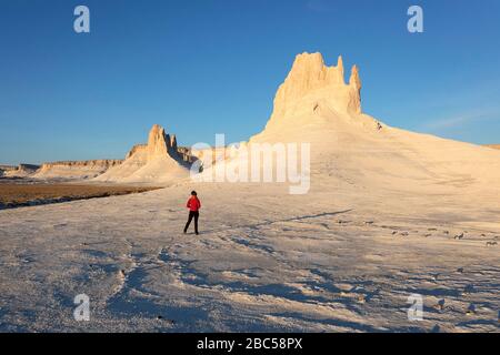 Frau in roter Jacke stehend und Blick auf Kalksteinberge, Ustyurt, Boszhira, Kaspische Depression Wüste, Aktau, Mangystau, Kasachstan Stockfoto