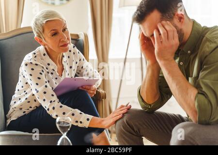 Der ernsthafte professionelle Psychologe beugt sich einem depressiven Mann Stockfoto