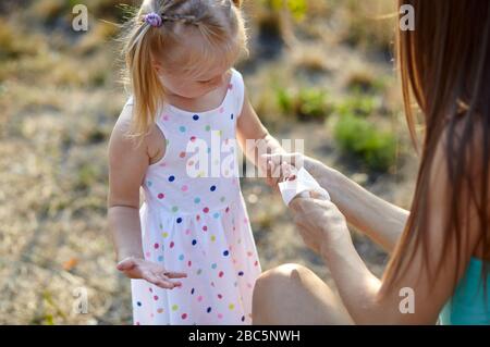 Mama wischt die Handfläche ihrer Tochter mit einer feuchten Serviette. Mutter kümmert sich um ihre kleine Tochter. Schutz vor Corona-Virus-Pandemie durch Händewaschen Stockfoto