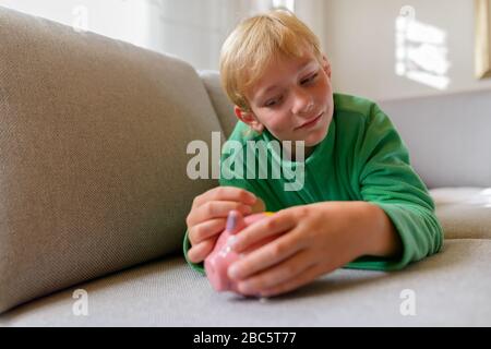 Junger gutaussehender Junge, der zu Hause eine Münze auf der Schweinebank einsteckte Stockfoto