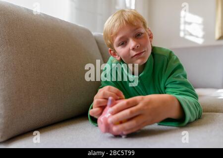 Junger gutaussehender Junge, der zu Hause eine Münze auf der Schweinebank einsteckte Stockfoto