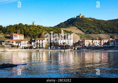 Collioure, Frankreich - 24. Februar 2020: Strandhotels in Collioure Village mit Windmühle auf Hügel, Roussillon, Vermilion-Küste, Frankreich. Es ist eine Oase der Künstler Stockfoto