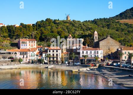 Collioure, Frankreich - 24. Februar 2020: Strandhotels in Collioure Village mit Windmühle auf Hügel, Roussillon, Vermilion-Küste, Frankreich. Es ist eine Oase der Künstler Stockfoto