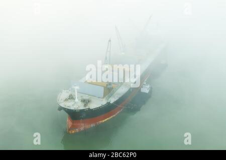 Der Bulk Aquila Massengutfrachter wird von Kohle auf Verankerung des Hafens Beringovskiy im Nebel beladen. Stockfoto