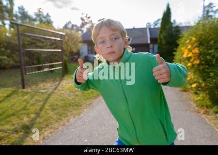 Junger gutaussehender Junge, der im Vorgarten Daumen nach oben gibt Stockfoto