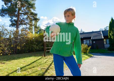 Junger gutaussehender Junge, der denkt, während er Fußball im Vorgarten hält Stockfoto