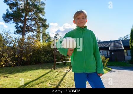 Fröhlicher junger gutaussehender Junge, der im Vorgarten Fußball hält Stockfoto