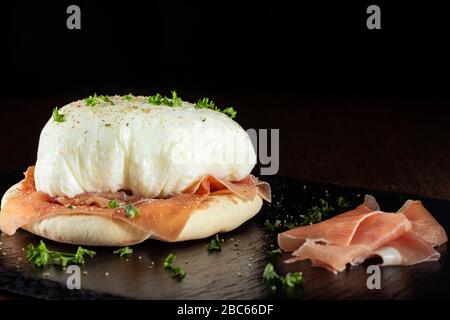 Pochierte Eier mit parmaschinken und Brot auf dunklem Schiefer Stockfoto