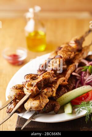 Traditionelles Schashlik auf einem Grillspieß mit Gemüse in der Nähe von Tomatensauce und Öl auf einem schwarzen Holzbrett im Restaurant. Keto oder Paleo Diät Stockfoto