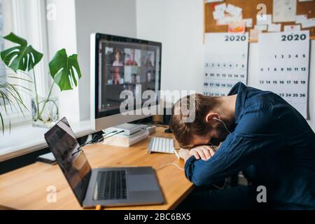 Müde Geschäftsmann schläft auf seinem Schreibtisch, während ein Videoanruf über einen Computer im Home Office. Bleiben Sie zu Hause und arbeiten von zu Hause Konzept durin Stockfoto