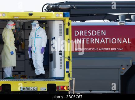 02. April 2020, Sachsen, Dresden: Medizinisches Personal steht beim Eintreffen eines Rettungsflugzeugs mit einem schwer erkrankten Covid 19-Patienten aus Frankreich in einem Krankenwagen am Internationalen Flughafen Dresden. Das Flugzeug Learjet 45 kam aus Metzger und landete am Nachmittag auf dem Flughafen Dresden. Wie das Universitätsklinikum Dresden auf Anfrage mitteilte, werden am Abend zwei weitere französische Patienten erwartet. Das Fachkrankenhaus Coswig, das Krankenhaus Dresden-Friedrichstadt und das örtliche Universitätsklinikum würden jeweils einen der Patienten versorgen. Über ihre Identität wurde nichts enthüllt. Sachsen hatte bereits a Stockfoto