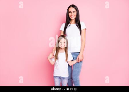 Foto der attraktiven jungen Mutter kleine Tochter zwei Damen gute Laune Stand nah Beste Freunde halten Arme tragen Freizeit weiße T-Shirts Jeans isoliert Stockfoto