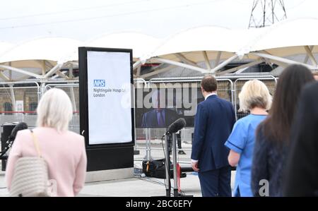 Gäste, darunter Gesundheitsminister Matt Hancock (Center), sehen sich bei der Eröffnung des NHS Nightingale Hospital im Excel Center in London eine Videobotschaft des Prince of Wales an, der als "Duke of Rothesay While in Scotland" bekannt ist. Ein temporäres Krankenhaus mit 4000 Betten, das für die Behandlung von Covid-19-Patienten eingerichtet wurde. Stockfoto