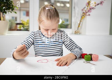 Hübsches Mädchen, das Hausarbeit während der Quarantäne verführt, Stickereien mit farbigen Fäden 3 Stockfoto