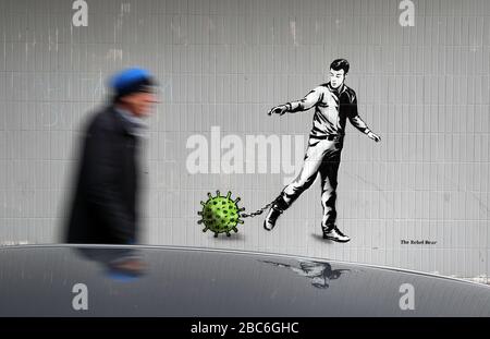 Eine Person geht an einem Kunststück des Künstlers vorbei, das als Rebel Bear bekannt ist, nachdem es an einer Wand in der Bath Street in Glasgow auftauchte. Die neue Ergänzung zu Glasgows Straßenkunst erfasst die globale Coronavirus Krise. Das Stück zeigt einen Mann, der eine Kette mit einem daran befestigten Keim zieht, während Großbritannien sich in einem Lockdown fortsetzt, um die Ausbreitung des Coronavirus einzudämmen. Stockfoto